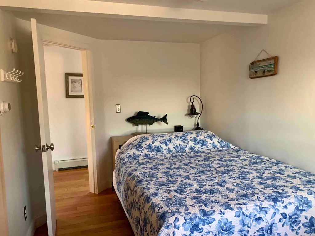 Bedroom with blue-and-white floral bedding, a fish ornament, bedside lamp and wood floor.